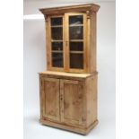 A pine tall bookcase, the upper part with three adjustable shelves enclosed by pair of glazed doors,