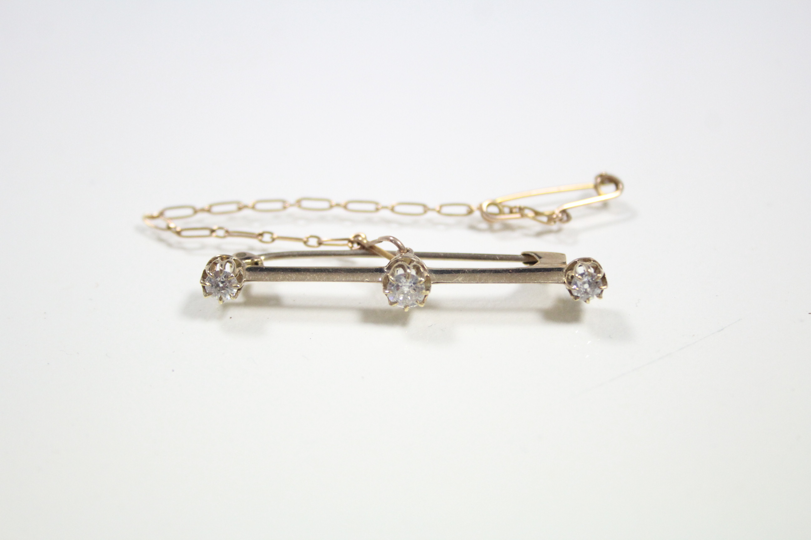 A yellow metal knife-edge bar brooch set three diamonds, the centre stone approximately 0.25 carats;