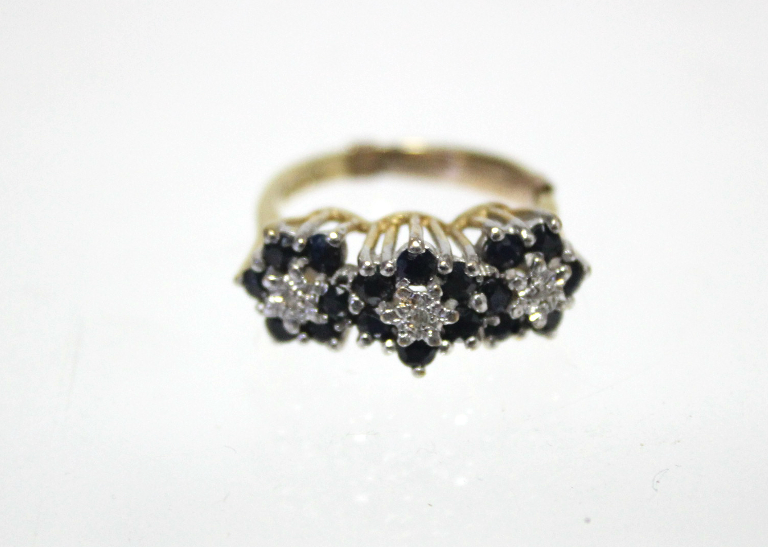 An 18ct. gold ring set three small diamonds, each within a border of small sapphires; London