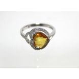 A white 14K ring set heart-shaped yellow sapphire within a border of small diamonds.