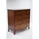 An early 19th century mahogany bow-front chest of four long drawers with pressed brass oval sewing
