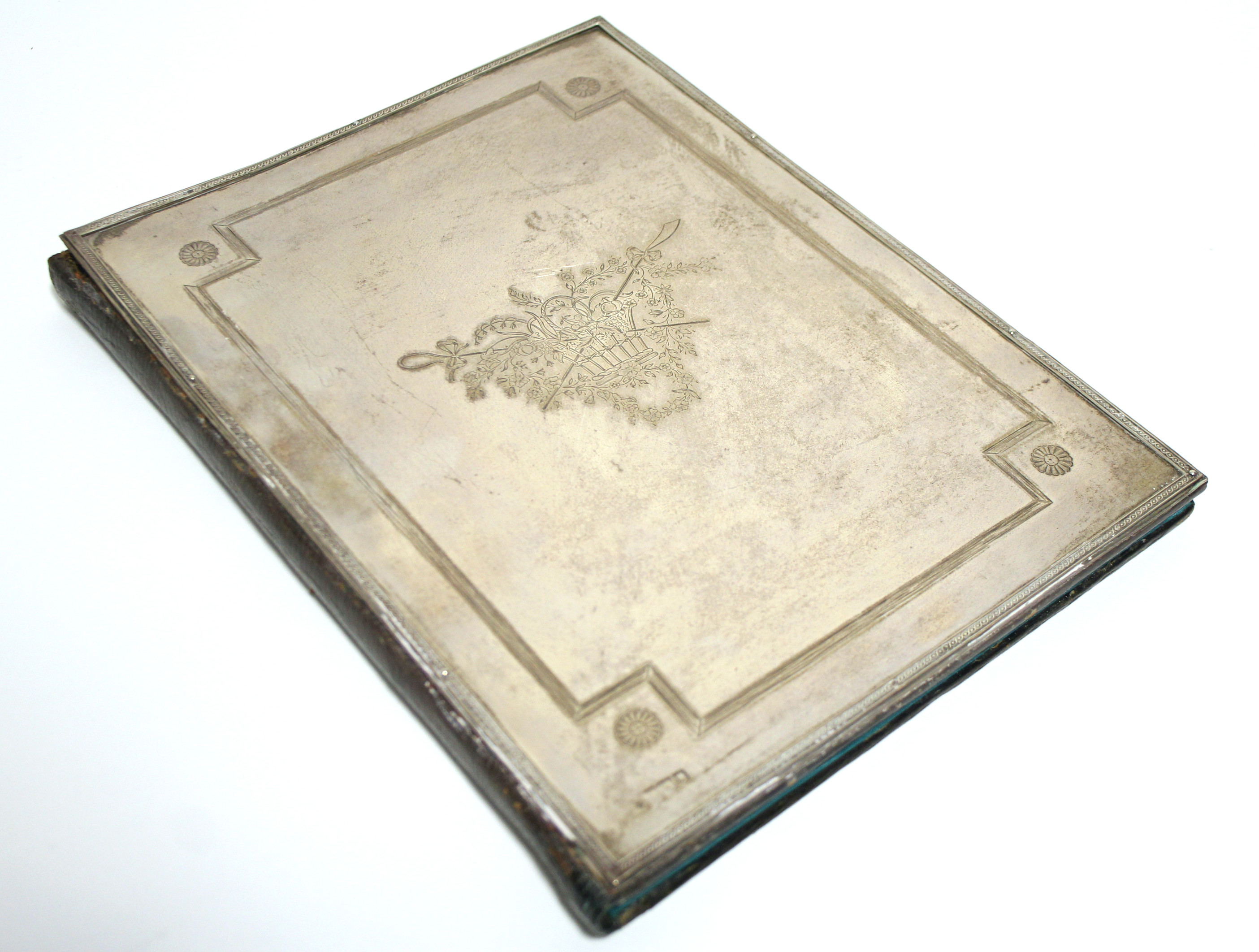 A rectangular leather blotter, the front with applied silver cover engraved with a basket of