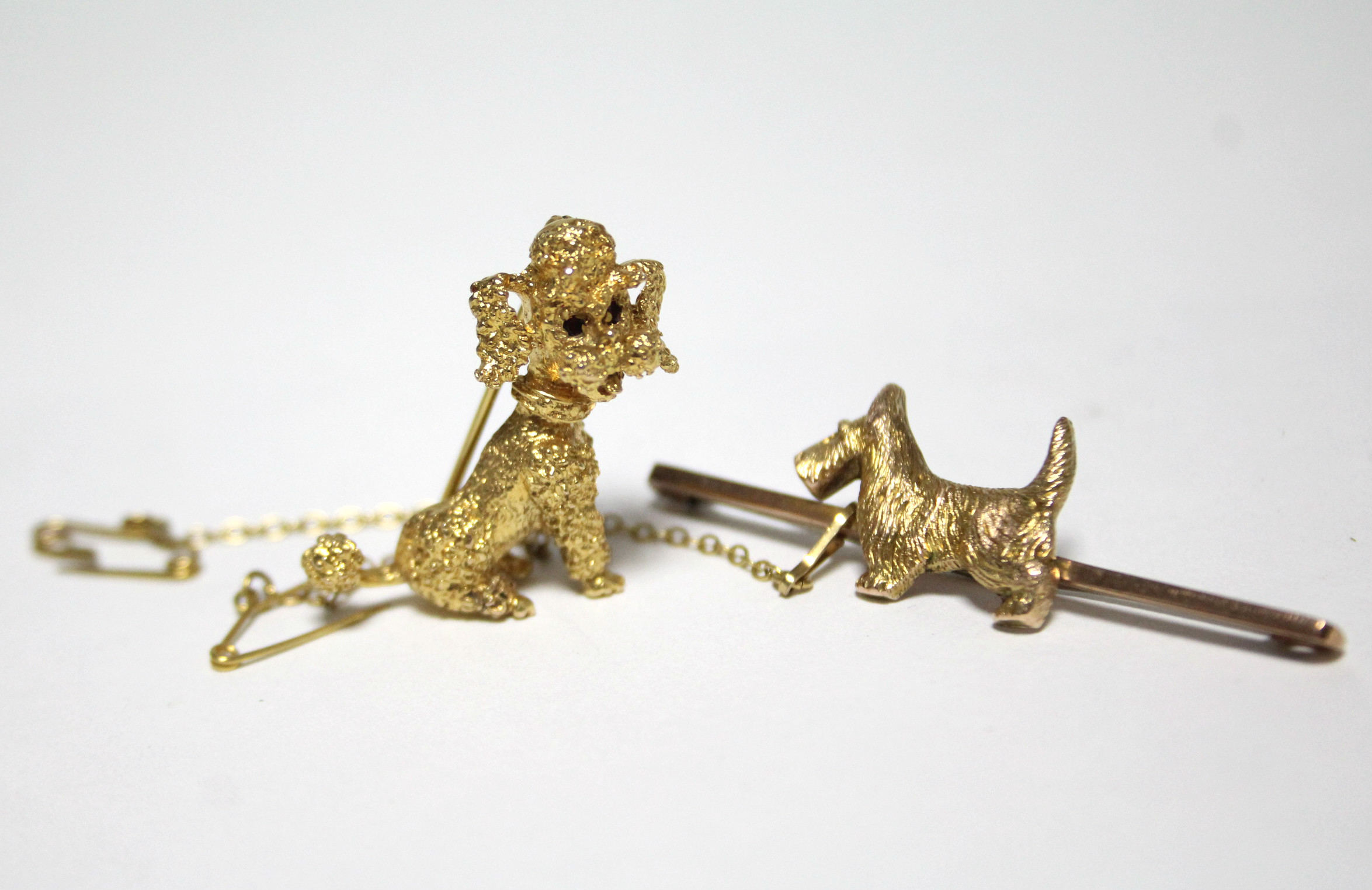 A cast 9ct. gold brooch in the form of a seated Poodle inset red gemstone eyes; a 9ct. gold