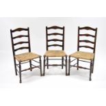 A set of three Lancashire-type oak ladder-back dining chairs with rush seats, on turned centre