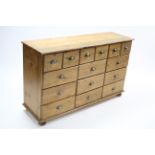 A pine chest fitted with an arrangement of fifteen drawers, &on bun feet, 52½" wide.