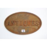 A reproduction cast-iron oval sign "ANTIQUES", 8¼" x 13½".
