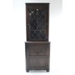 A reproduction carved oak tall standing corner cabinet, the upper part fitted two shelves enclosed