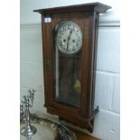 A 1920s light oak cased wall clock with glazed panels and a full height door;