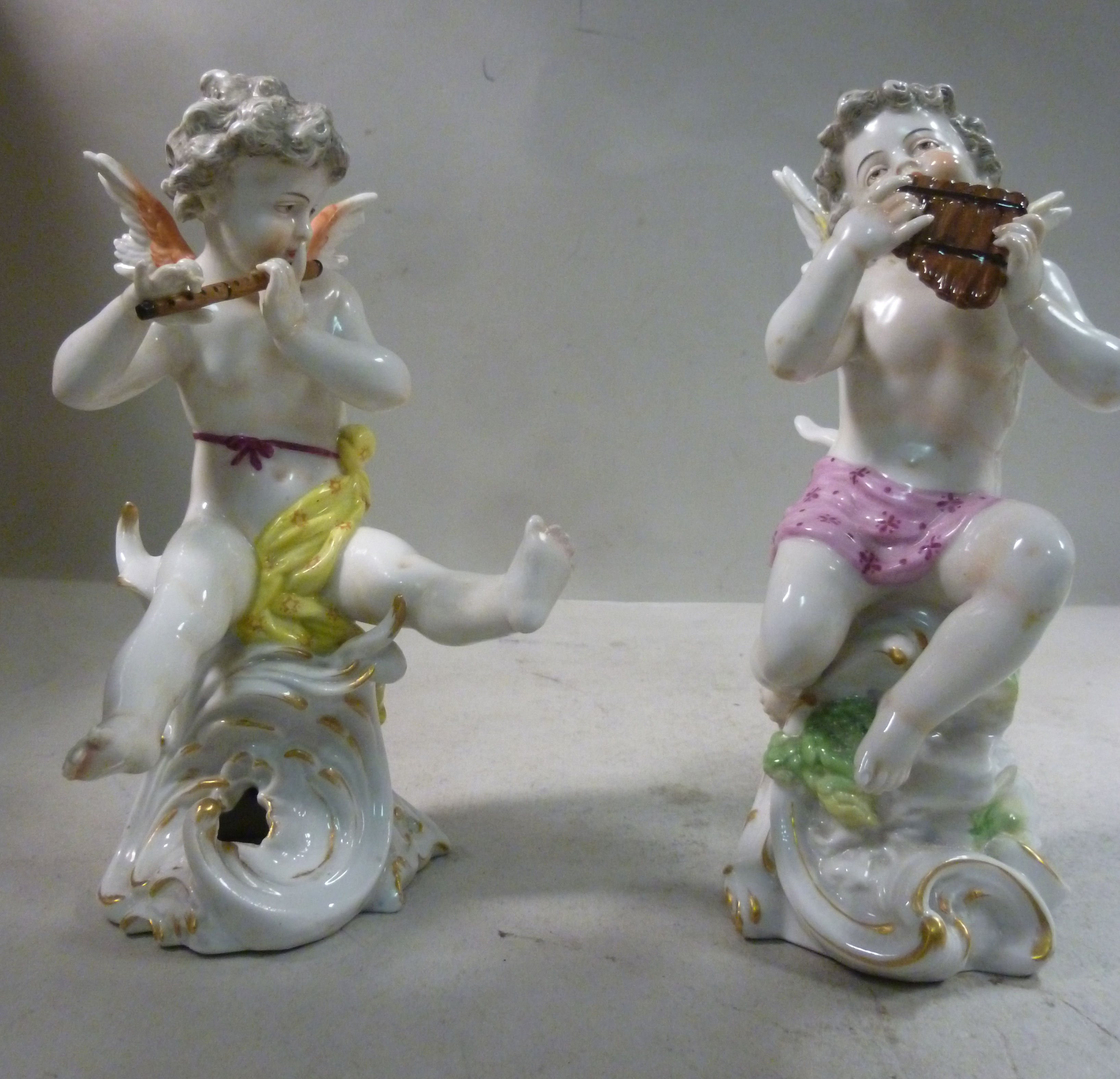 A pair of early 20thC Frankental porcelain seated cherubic figures, one playing panpipes,