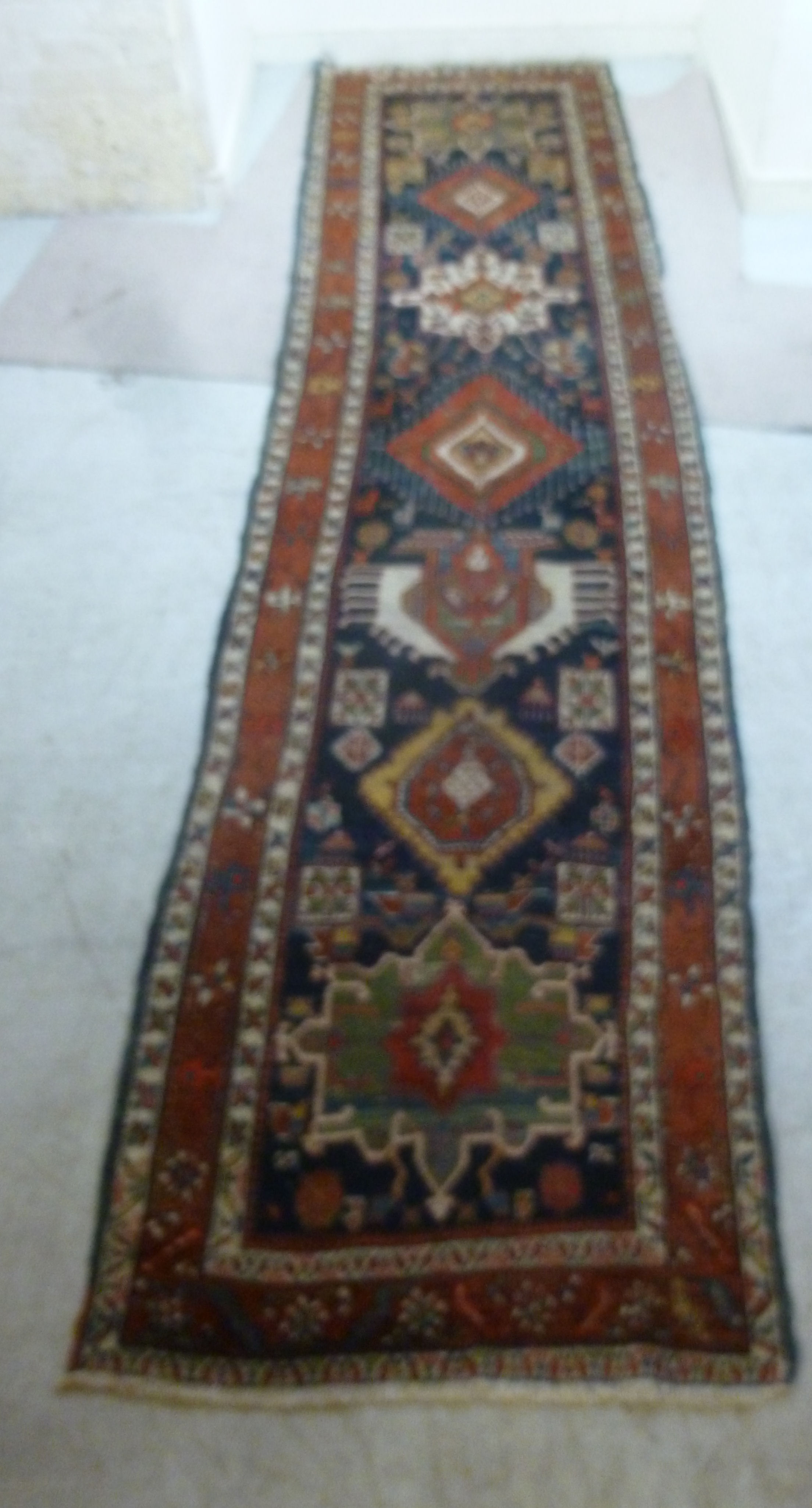 A Caucasian runner with repeated stylised diamond motifs on a blue and red ground 154'' x 39''