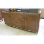 An Ercol Golden Dawn elm sideboard with three central drawers, flanked by a pair of cupboard doors,