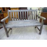 A modern teak garden bench with a level back and swept arms,