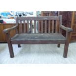 A modern teak garden bench with a level back and swept arms,