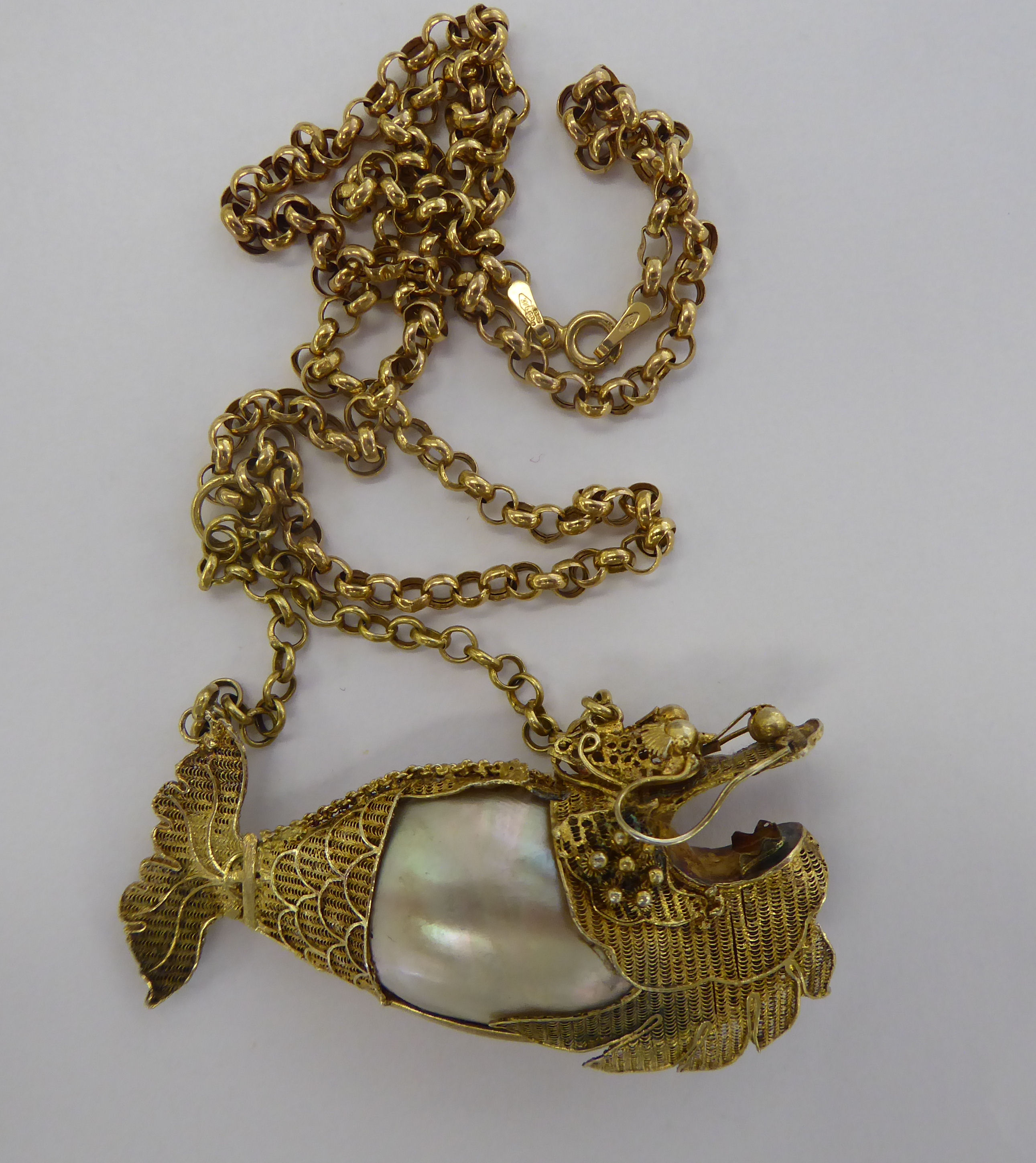 A yellow metal and seashell pendant, fashioned as a fish,