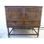 A George III oak cabinet-on-stand with a planked top, over two panelled doors and two drawers,