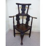 A mid 19thC oak framed corner chair, ornately carved with mask motifs, fruiting vine and flora,