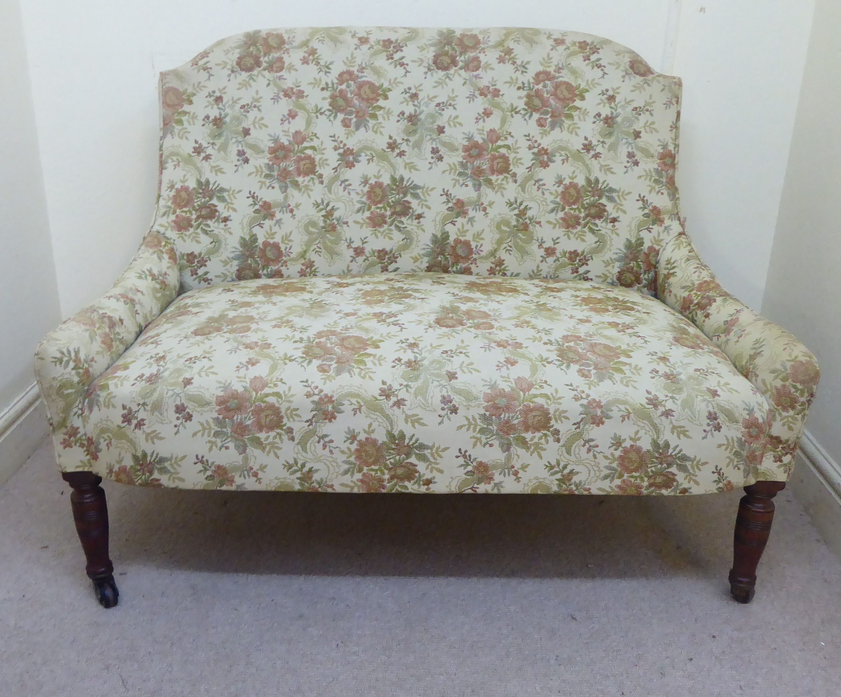 A late Victorian small salon settee, upholstered in a beige coloured, floral fabric,