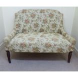 A late Victorian small salon settee, upholstered in a beige coloured, floral fabric,