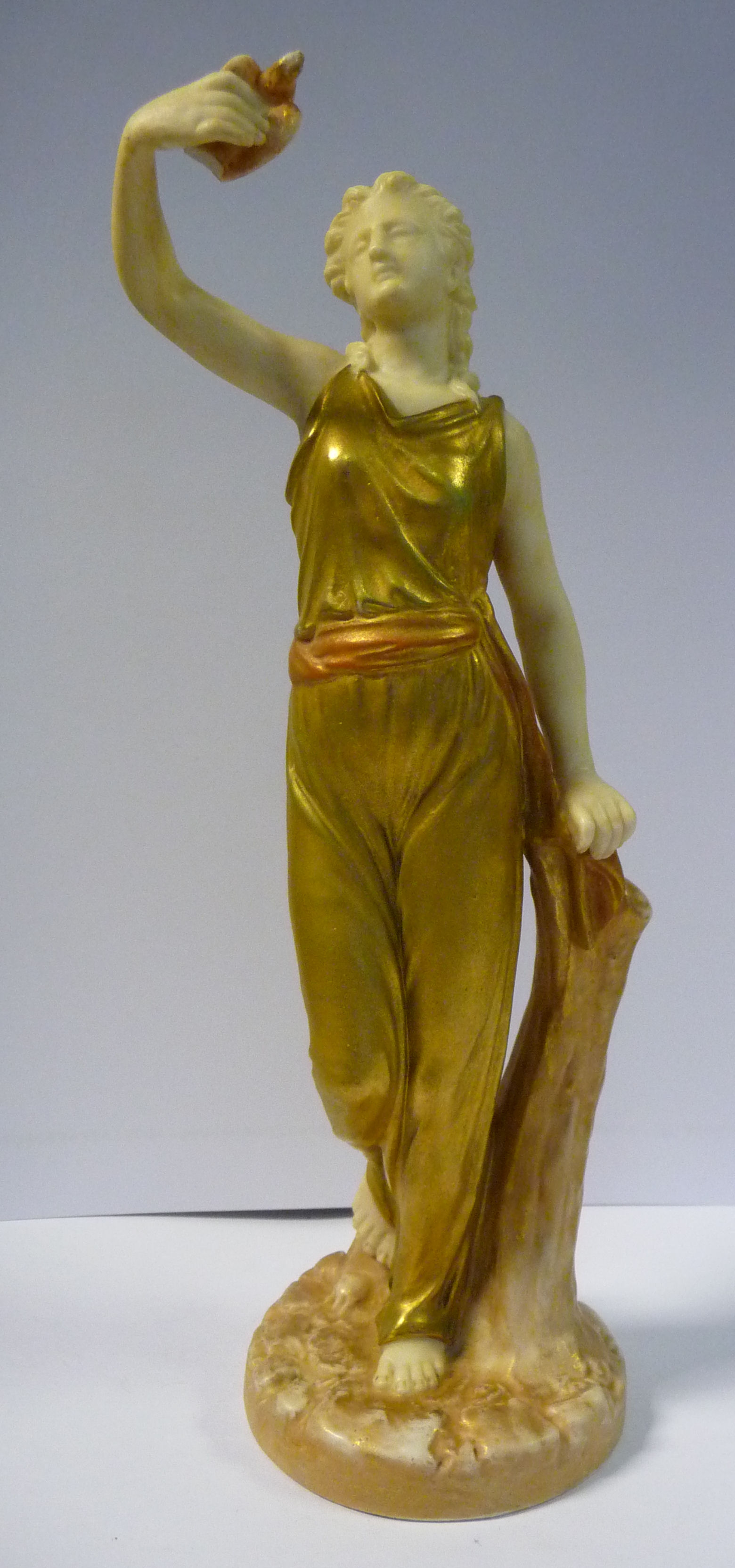 A Royal Worcester gilded and painted satin glazed china figure, a woman holding a dove,