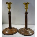 A pair of early 19thC turned mahogany candlesticks, each with a cast brass socket and flared sconce,