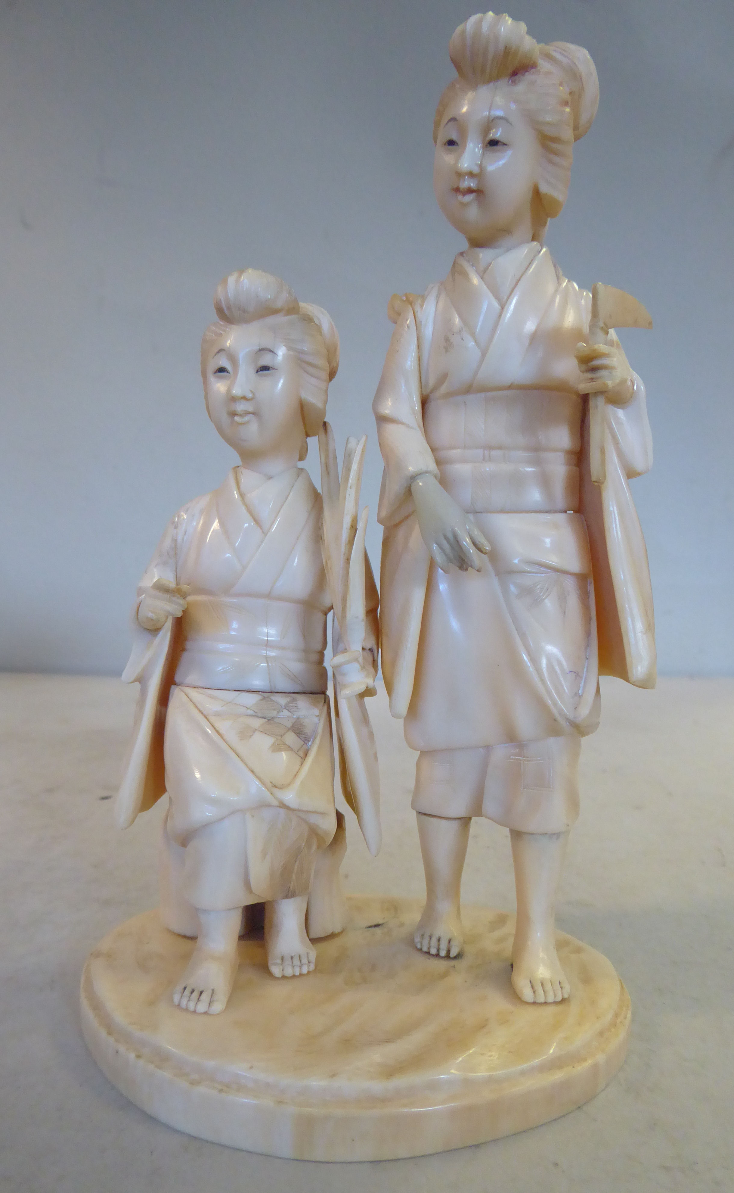 An early 20thC Japanese carved ivory artisan group, two women, one standing, the other seated,