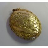 A mid Victorian gold coloured metal oval locket with C-scrolled and foliate engraved ornament