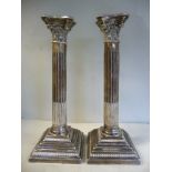 A pair of silver candlesticks of square outline, each socket within an incurved Corinthian capital,