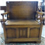 A mid 20thC stained oak monk's bench with a hinged seat, panelled front,