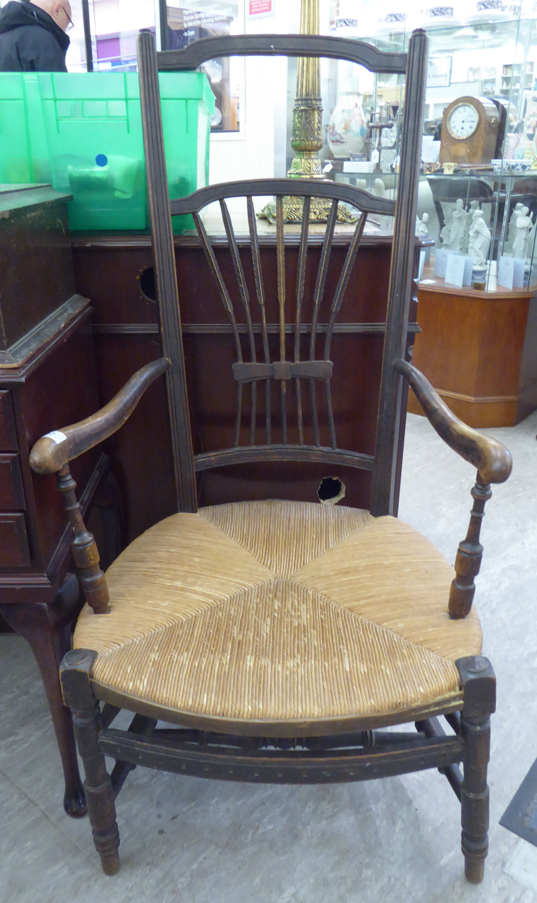 An early 20thC stained beech framed elbow chair with a wheatsheaf carved splat,