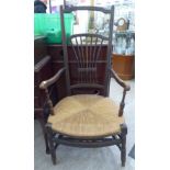 An early 20thC stained beech framed elbow chair with a wheatsheaf carved splat,