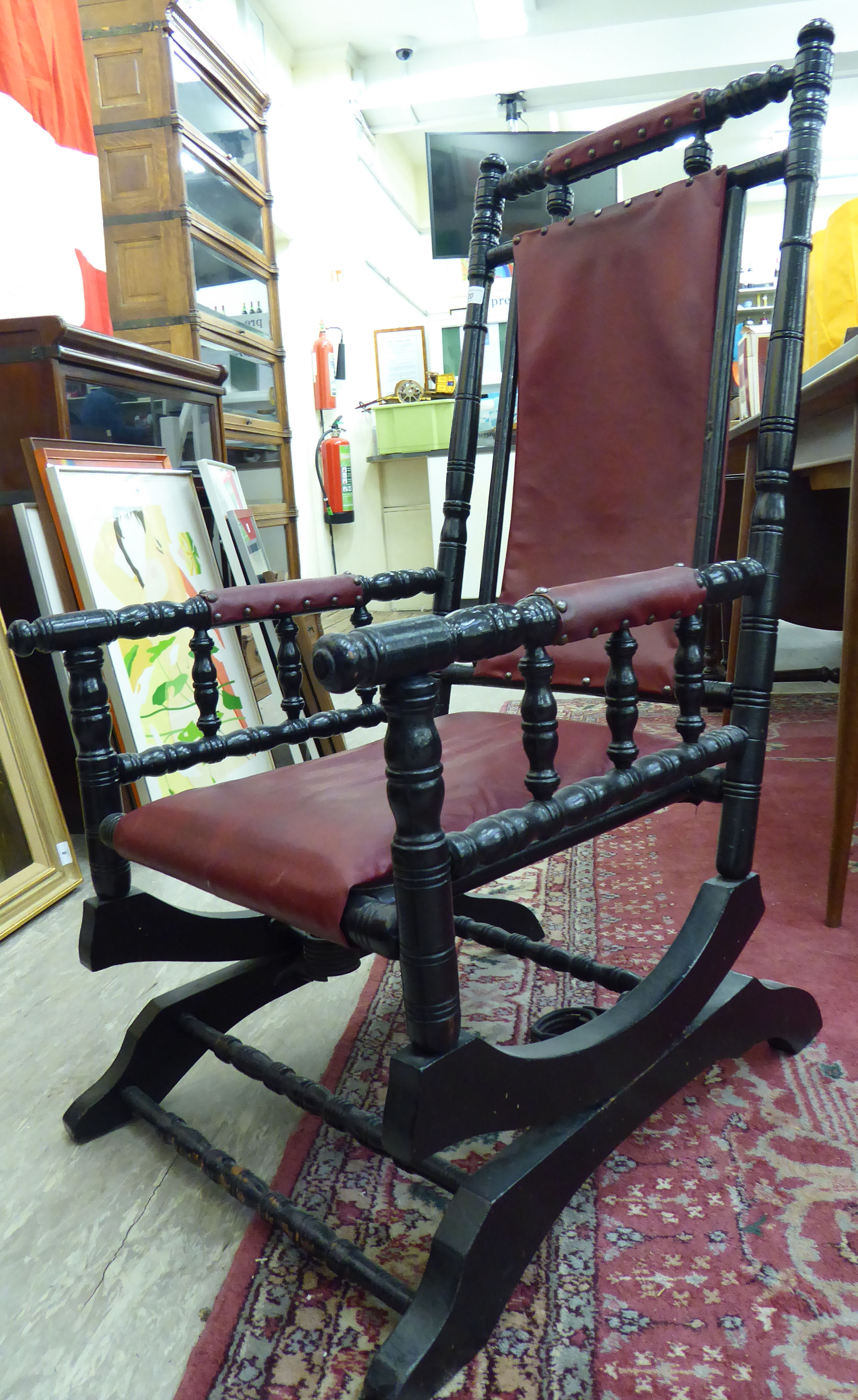 A late 19thC American design ebonised hardwood framed rocking chair with a red faux hide