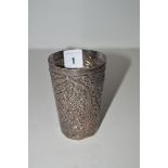 An Indian white metal beaker of tapering form, decorated with scrolling floral designs.