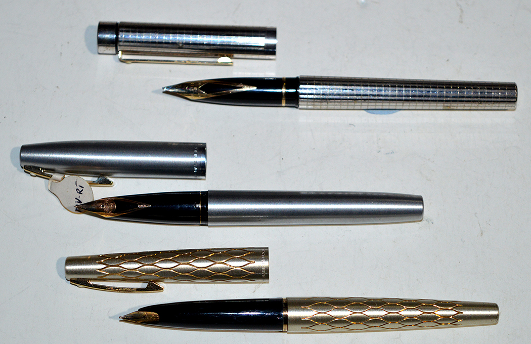 Three Sheaffer fountain pens, one in silver coloured case with gold decorated wave design,