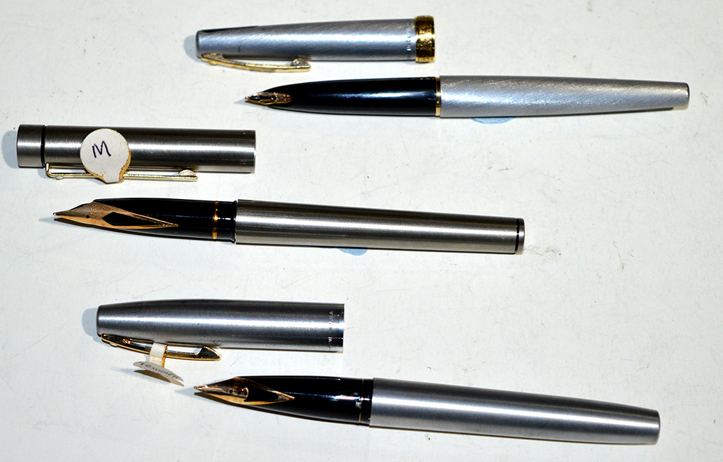 Three steel cased Sheaffer fountain pens, one with gold plated feather scroll collar,