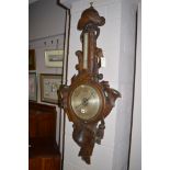 A Victorian carved oak barometer, decorated with a horn, hat and military trophies.