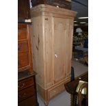 A stripped pine wardrobe, panel door above drawer below, raised on turned feet, 87cms wide.