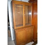 An early 20th Century display cabinet, close doors above cupboard doors, raised on cut-away base,