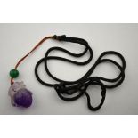 A Chinese carved amethyst pendant of animal on fruit strung on silk cord with green stone bead