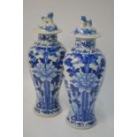 A pair of Chinese blue and white vases; each one with a domed cover and Buddhist Lion dog finial,