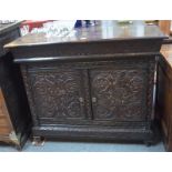 An unusual carved oak side cabinet with floral and foliage frieze above twin panelled doors,