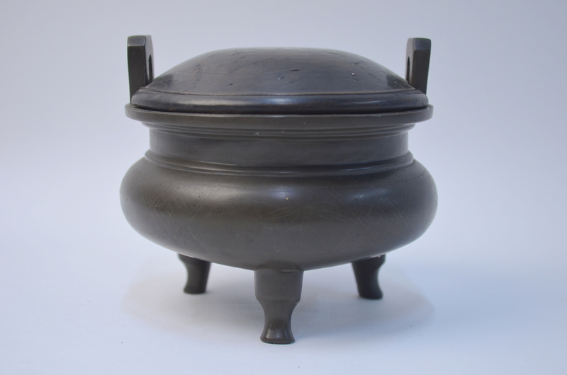 A metal incense burner of tripod and cylindrical form to/w an associated wood cover (2)