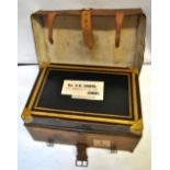 A japanned metal and gilt travelling trunk in tan leather case with travel label and label to top