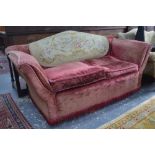 An old upholstered two seat arched back sofa having splayed arms and an ovoid needlepoint panel
