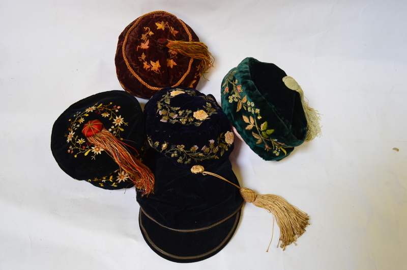 Five early 20th century smoking hats comprising; a black velvet floral embroidered hat with tassel,