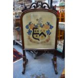 A Victorian rosewood firescreen with scrolling top above glazed panel set with a needlework coat of