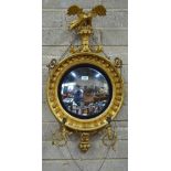 A Regency giltwood girandole convex mirror surmounted by a spreadwing eagle with scroll arm sconces,