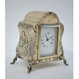 An Edwardian silver boudoir clock embossed with Watteausque picknickers, on scroll feet,