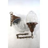 A pair of ovoid cut glass ceiling light shades with copper and brass tops and chains