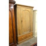 An antique pine wardrobe with panelled door enclosing a hanging rail and four slides over two