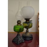 Two Victorian oil lamps with green glass reservoirs and metal bases (one with globe shade)
